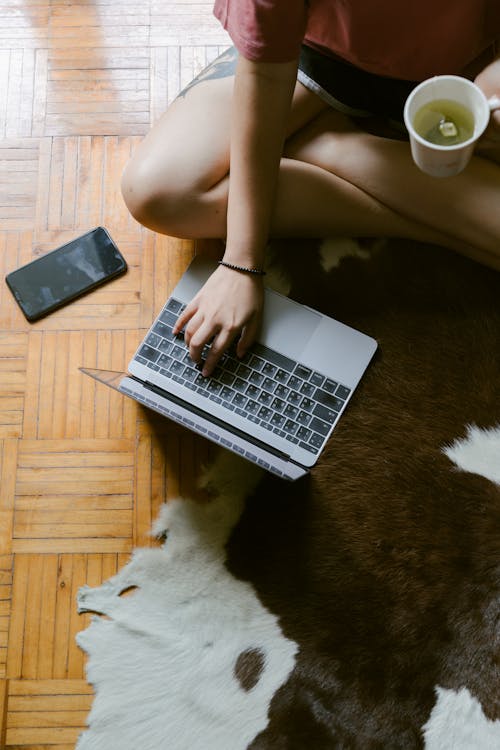 Free Anonymous woman typing on laptop studying on floor Stock Photo