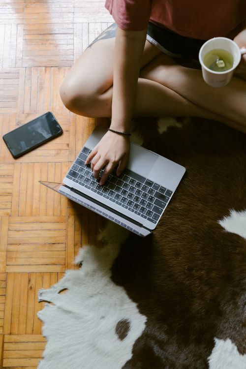 Free Top view of faceless female using laptop while sitting on floor with cozy carpet with cup of  green tea Stock Photo