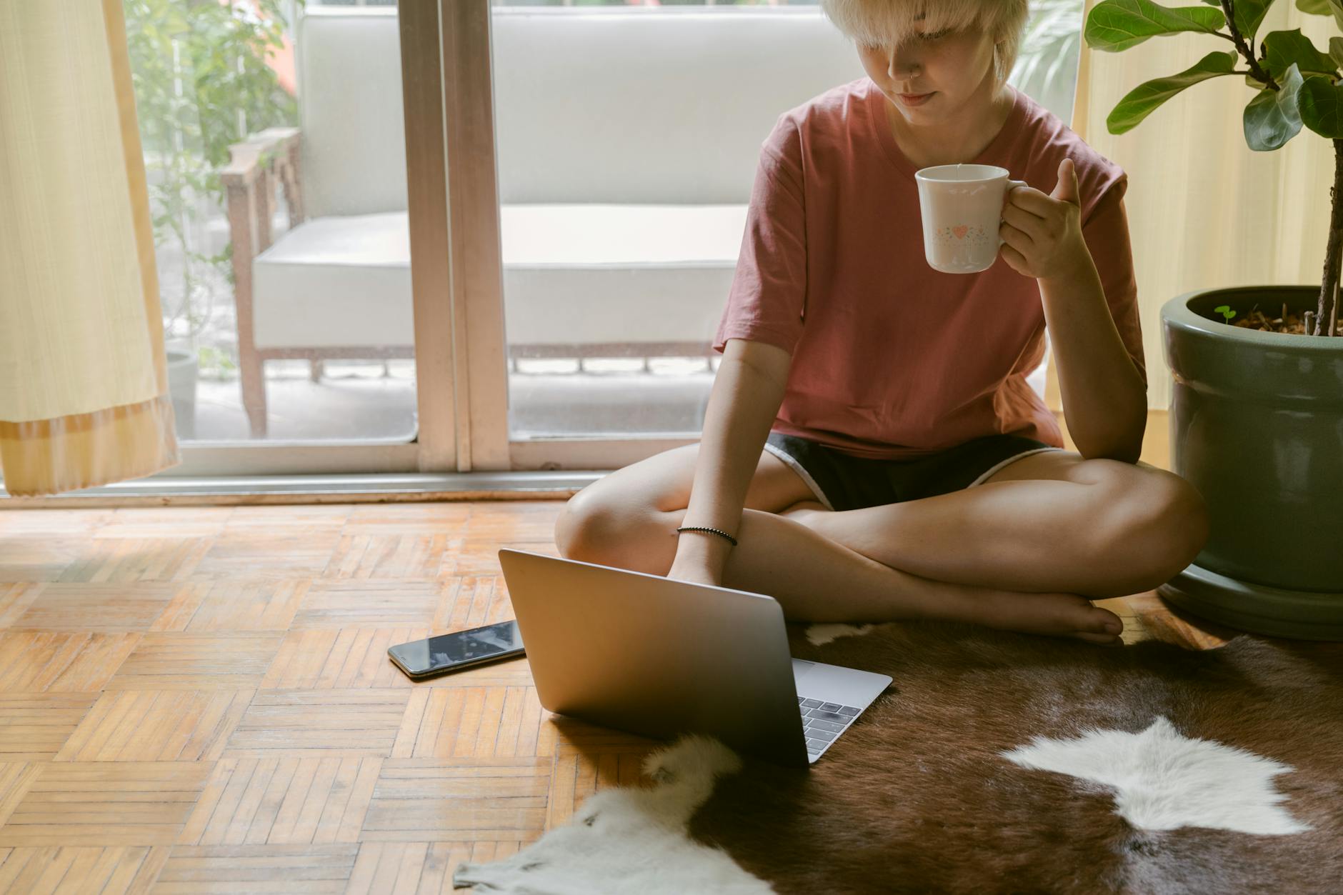 Woman sitting on floor drinking coffee and surfing on laptop 