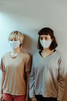 一位亚洲妇女在家戴着医用口罩，背靠白墙，正聚精会神地望向别处