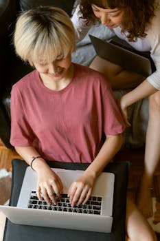 From above of crop young females in home clothes chatting in social media on laptops while spending time together at home