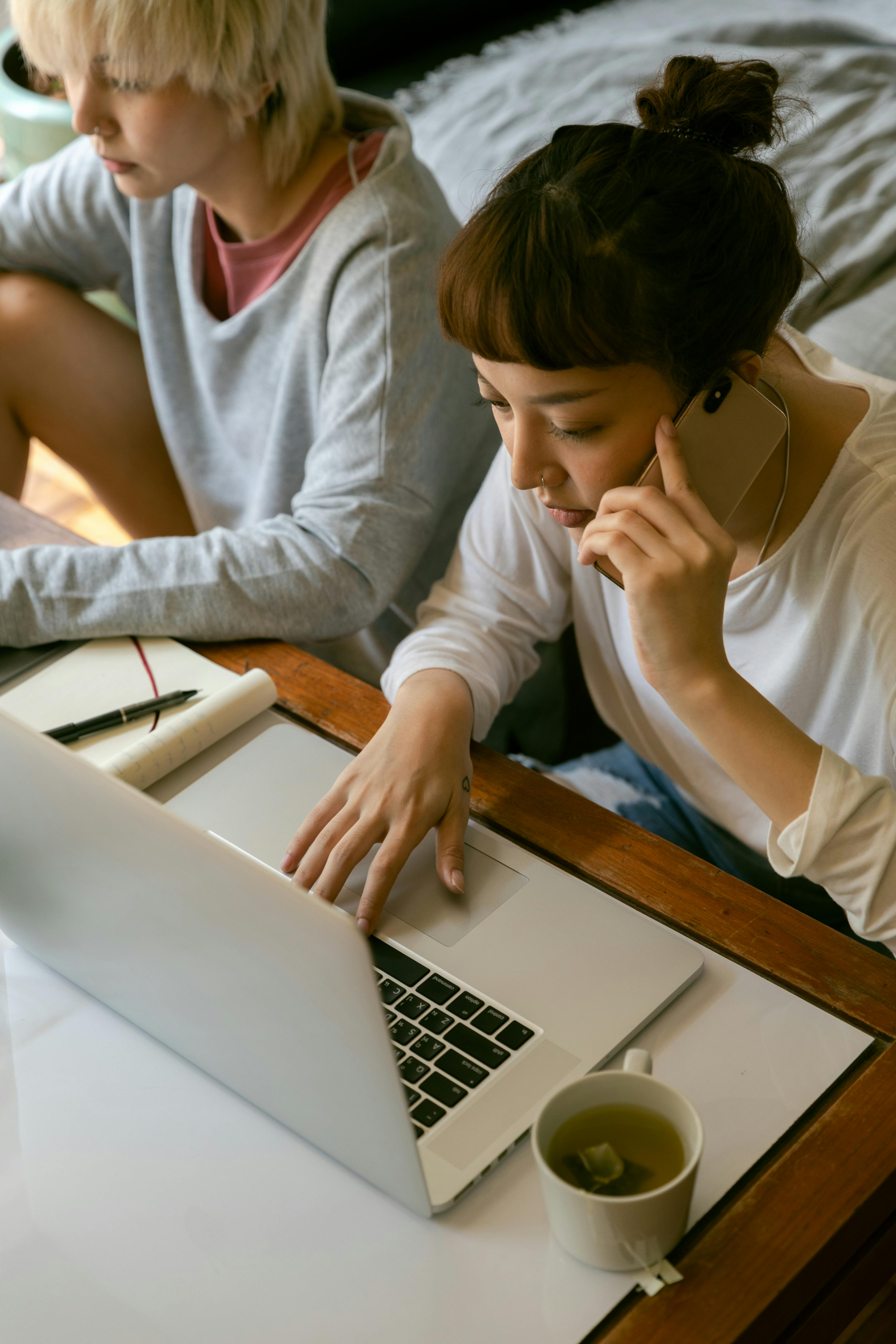 multiracial female girlfriends working on laptop and talking on smartphone