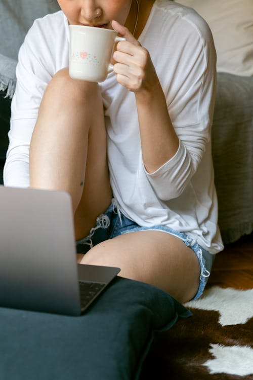 Crop unrecognizable female freelancer with laptop drinking tea at home