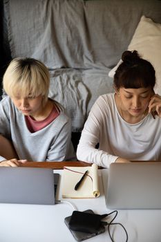 Top view of young multiracial female students in casual wear browsing internet on netbooks while sitting near copybook and hard drive in apartment
