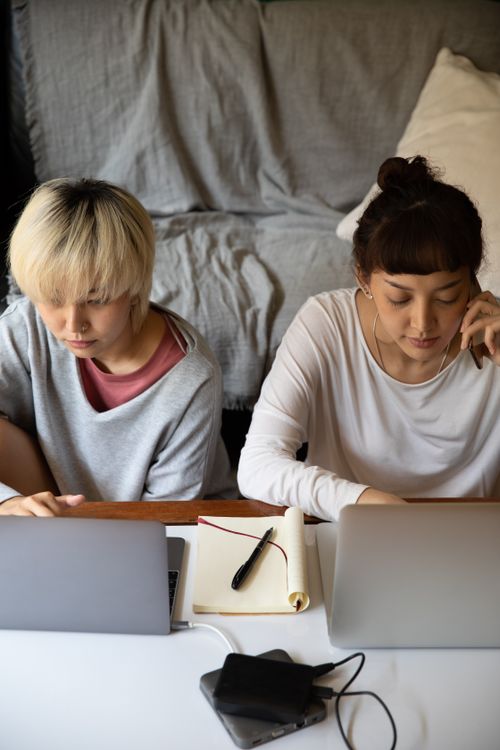 Free Top view of young multiracial female students in casual wear browsing internet on netbooks while sitting near copybook and hard drive in apartment Stock Photo