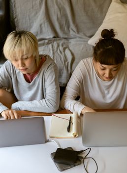 From above of young Asian girlfriends surfing internet on netbooks and connecting hard drives to computer while studying at home