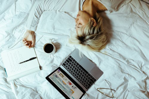 Student sleeping on bed near laptop and cup of coffee