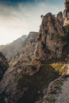 Majestic rocky cliffs of remote mountain range under cloudy sky in beams of sunlight
