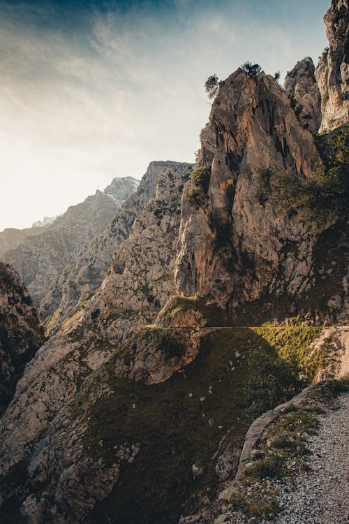 Majestic rocky cliffs of remote mountain range under cloudy sky in beams of sunlight