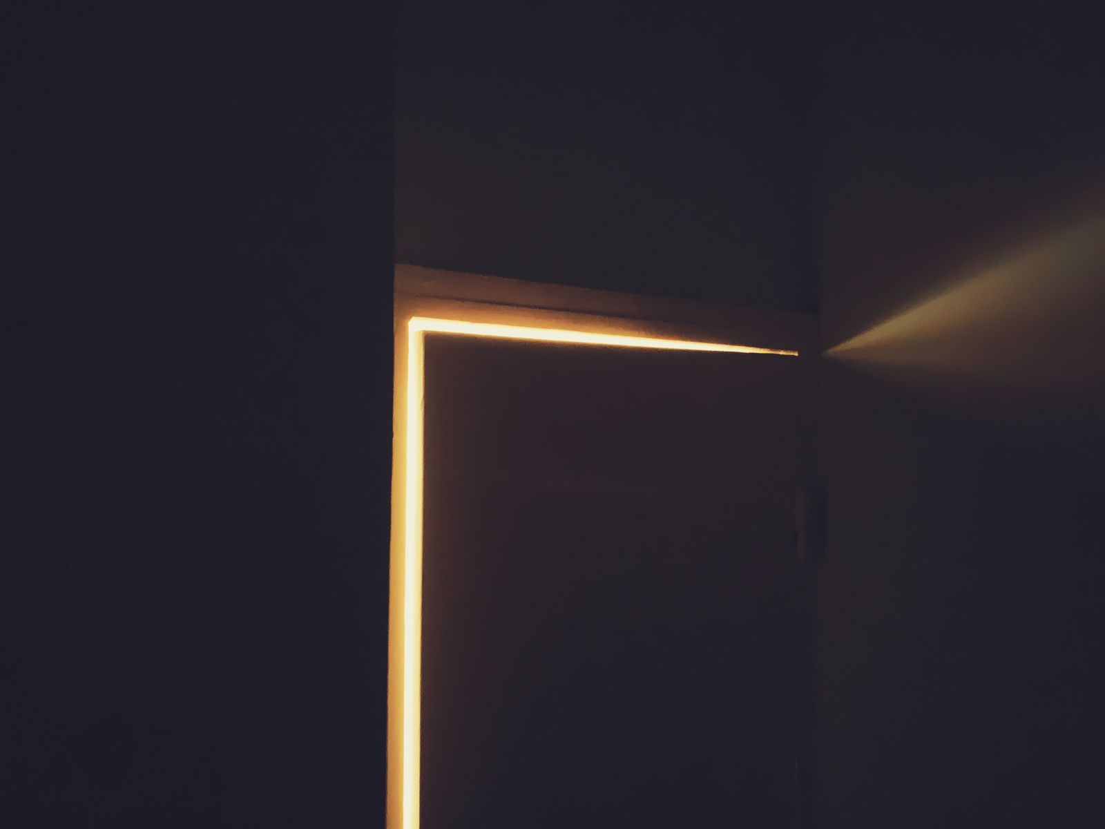 A door slightly ajar with warm light spilling through into a dark room