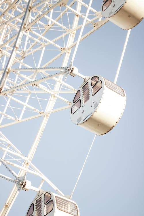 From below of modern white Ferris wheel with empty cabins against clear blue sky