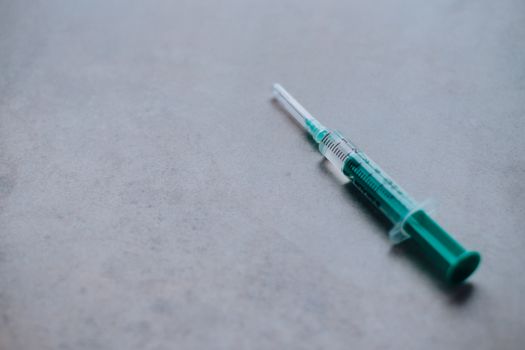 Close-up of a green syringe on a gray surface, ideal for health and medical themes.