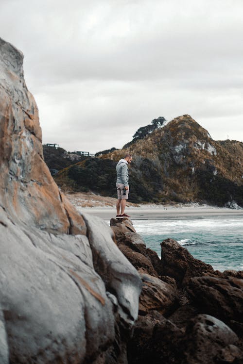 Free Man Standing on Rock Formation at Beach Stock Photo