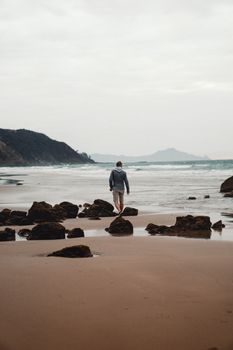一名男子独自在新西兰一处僻静的海滩上散步，四周岩石环绕，大海宁静