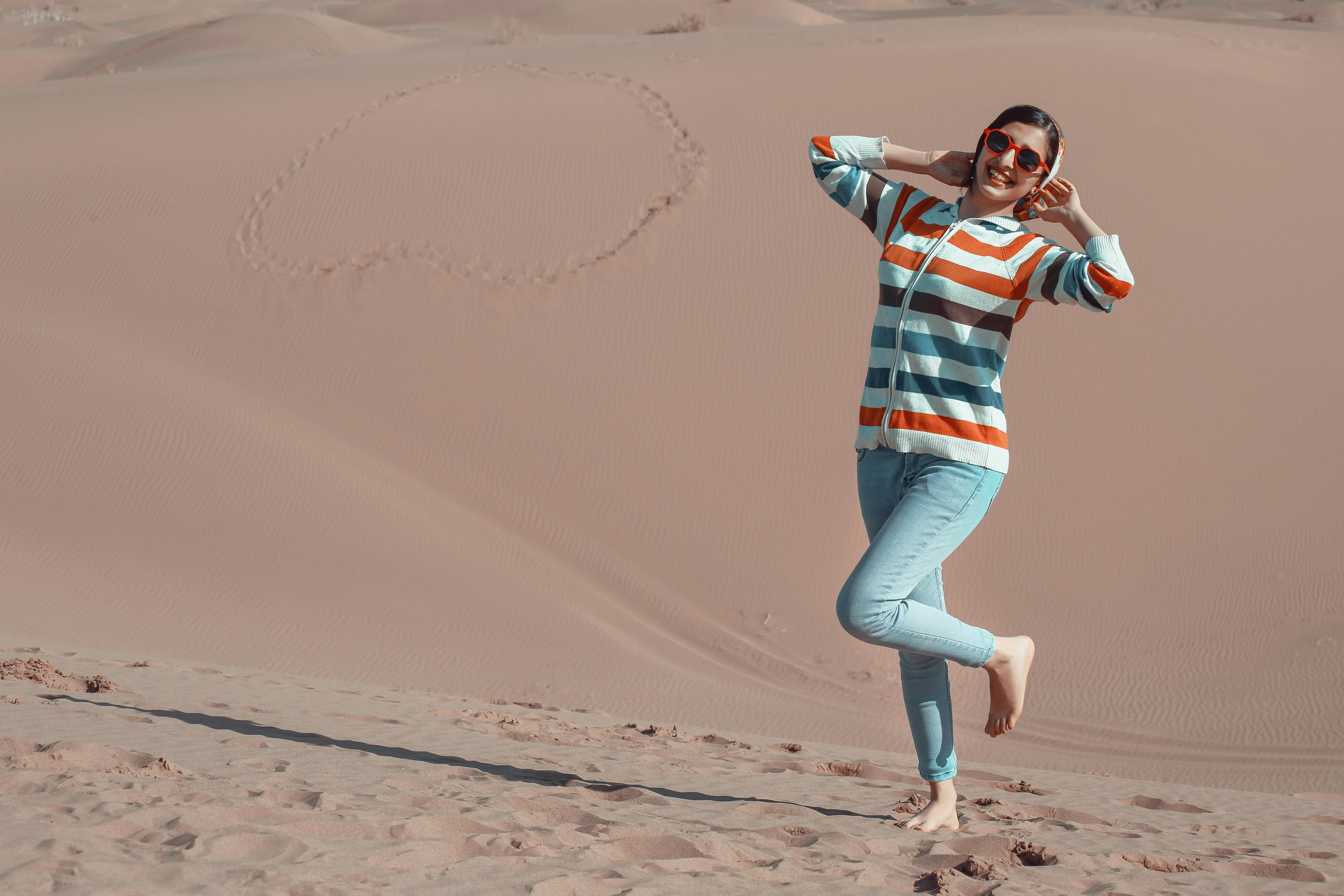 一名年轻女子赤脚在沙漠中快乐地摆着姿势，拥抱这无忧无虑的夏日