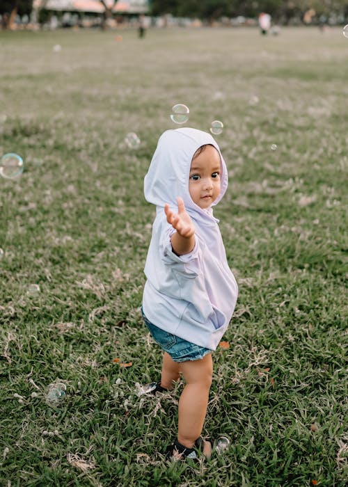Little child reaching arm in green field under soap bubbles