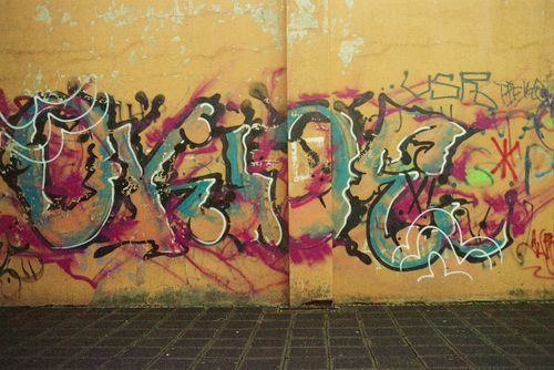 Free Painted artwork representing multicolored graffiti with letters and wavy messy lines on aged concrete wall near tiled pavement on city street in daylight Stock Photo
