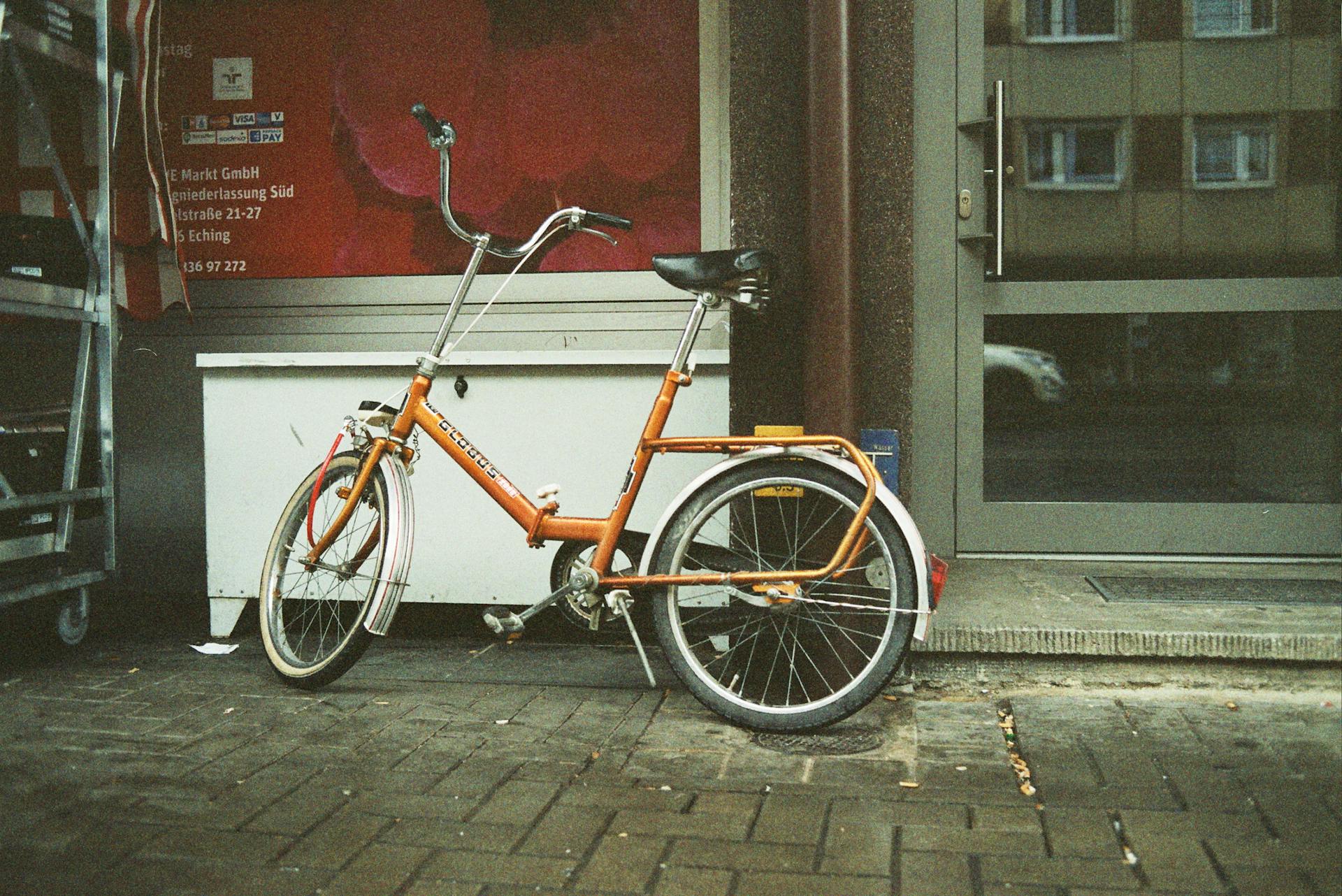 From above of aged bike with leather seat parked on shabby tiled street pavement near glass door reflecting building with windows in city in daylight