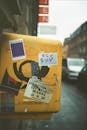 Old post box with stickers on city street with cars