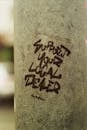 Old cement post with supportive inscription on shabby surface on city street in daylight on blurred background