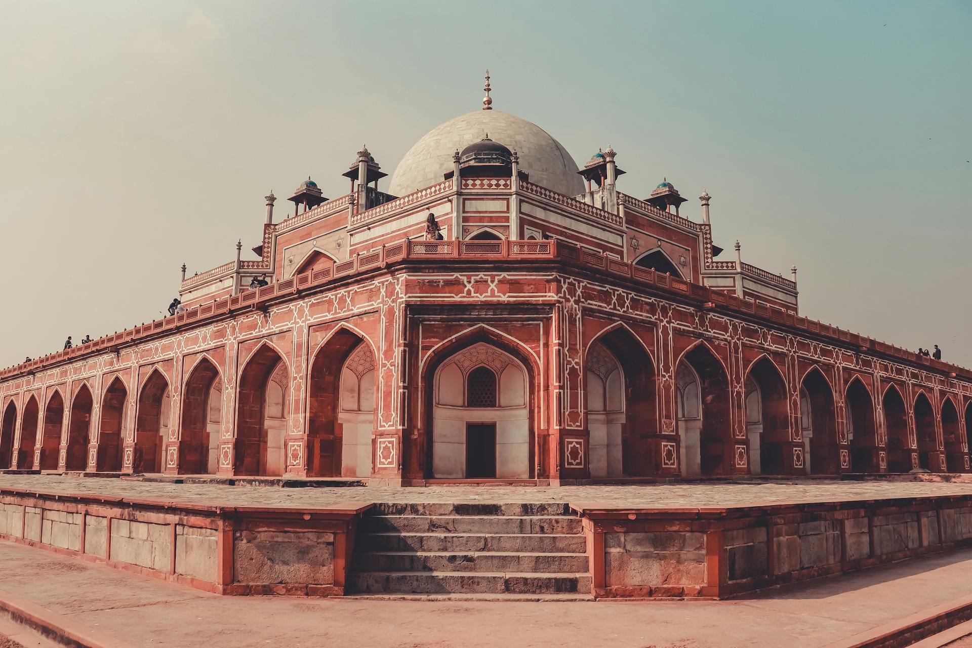 Facade of aged masonry Mughal style Tomb of Humayun with arched entrance near shabby staircase and dome on top in city with pavement in daylight