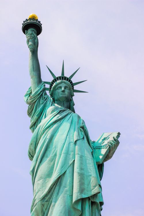 Free From below of old neoclassical style sculpture of Roman Goddess with spiky crown on head and raised arm with torch and tablet under sky in USA Stock Photo