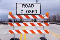 A road closed sign with barricade highlights caution on a suburban highway.