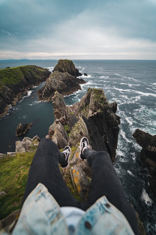 Free A Person Sitting on the Edge of a Cliff while Looking at the Beautiful View of the Sea Stock Photo