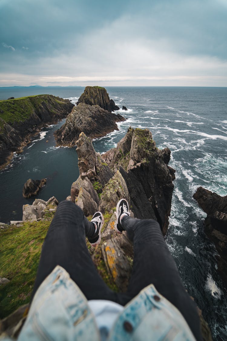 A Person Sitting On The Edge Of A Cliff While Looking At The Beautiful View Of The Sea