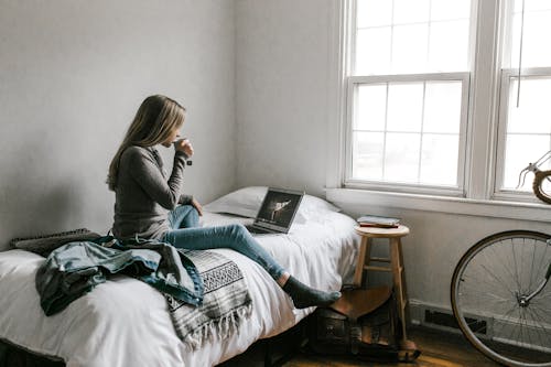 Woman in Gray Long Sleeve Shirt Sitting on Bed