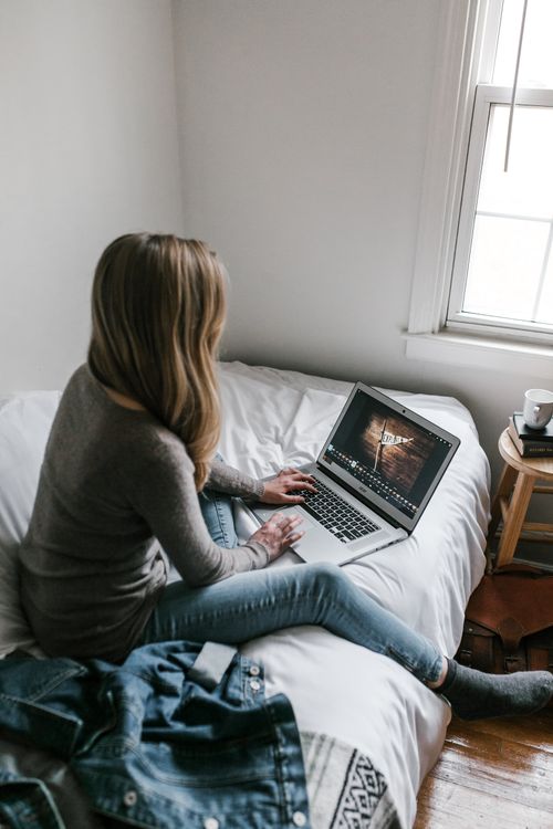 Free A young woman working from home on a laptop in a cozy, minimalist bedroom setting. Stock Photo