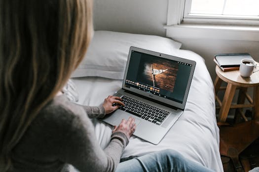 A young woman working remotely on a laptop in a modern bedroom setting.