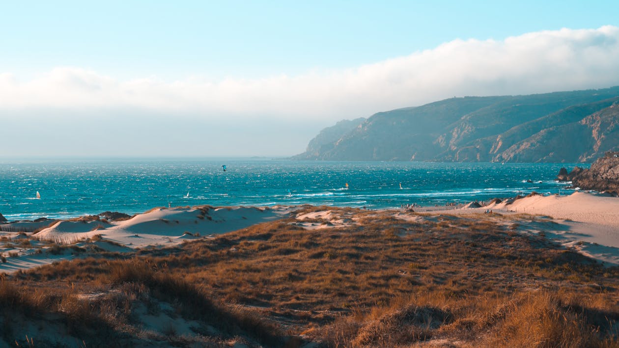 Endless ocean near mountains and sandy coast under cloudy sky