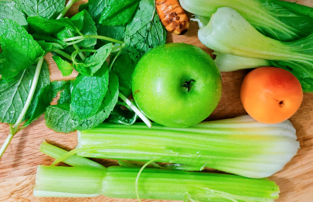 Celery, leafy greens, an apple and other fresh produce on a cutting board.
