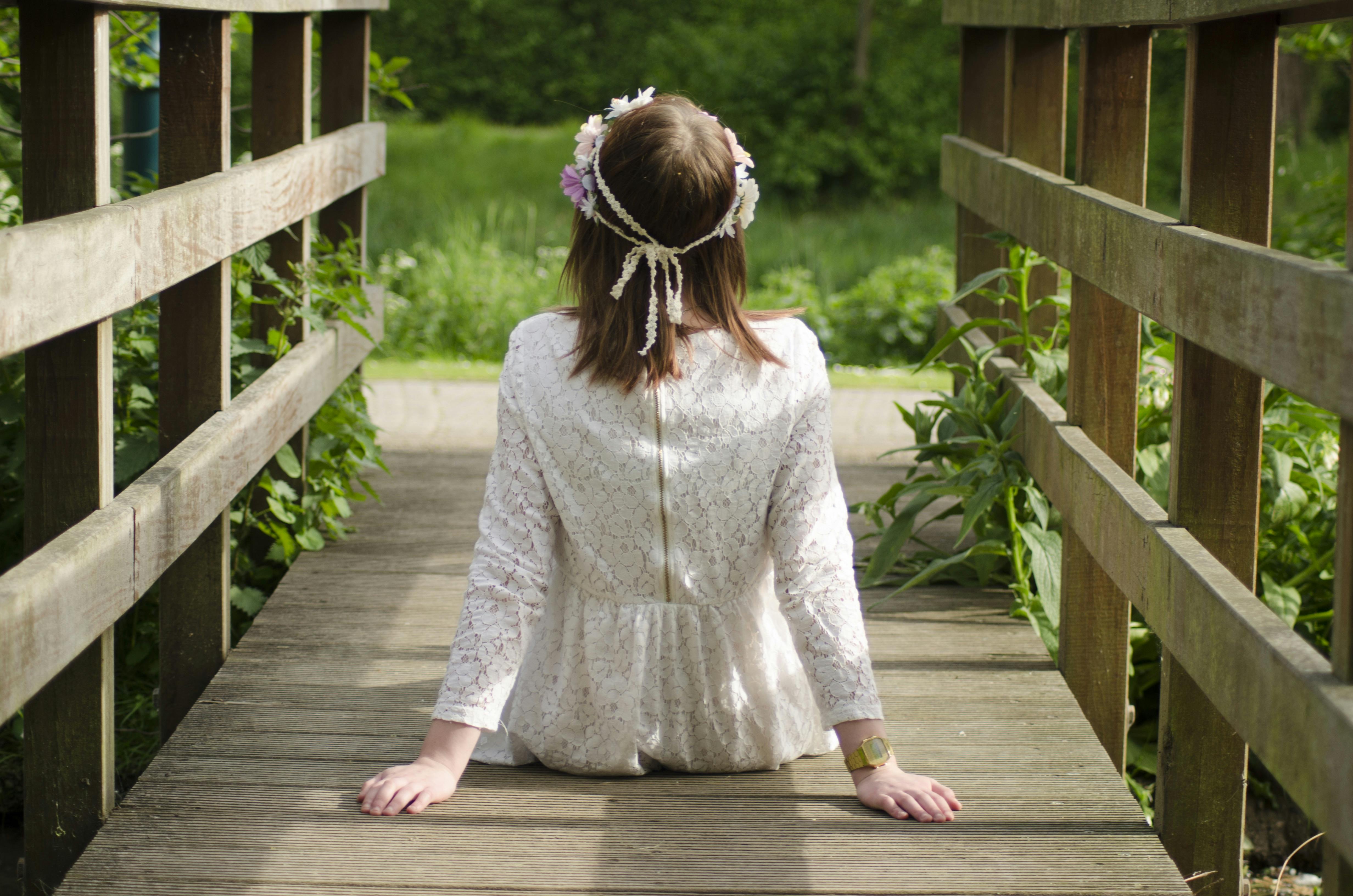 Free Back view of young woman with floral headband sitting outdoors on a wooden bridge. Stock Photo