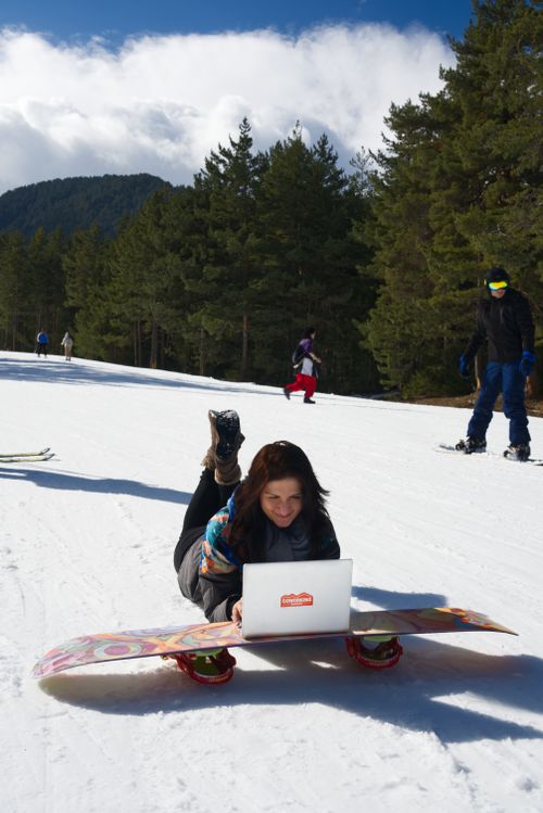 Free Woman using laptop on snowboard in snowy ski resort, embodying remote work lifestyle. Stock Photo
