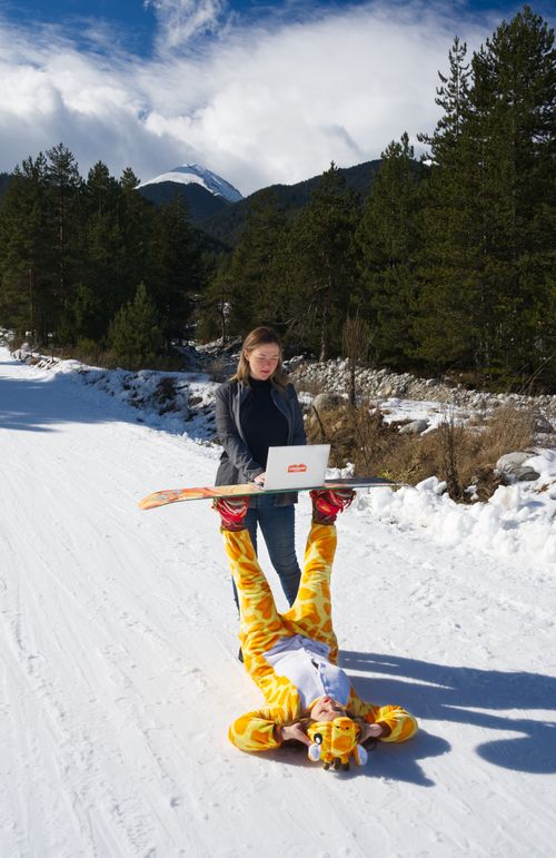 Free Woman using laptop supported by person in giraffe costume on snowy road in a ski resort. Stock Photo