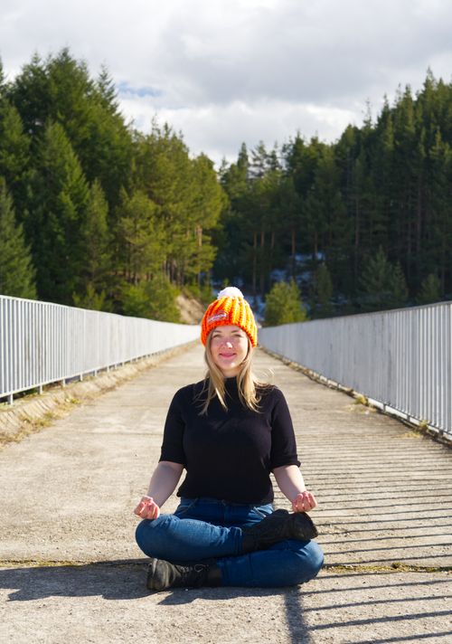 Free Young woman in a knit hat meditating on a bridge surrounded by nature. Stock Photo