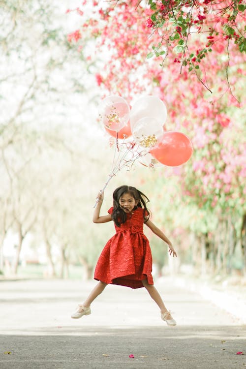 A Girl Jumping while Holding Balloons