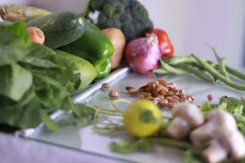 From above of various fresh organic colorful vegetables and nuts placed on glass tabletop in light kitchen