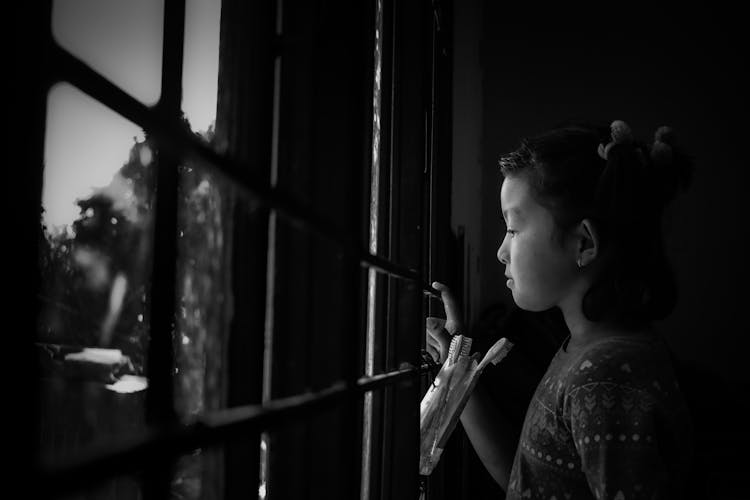 Thoughtful Ethnic Child Looking Through Window In Rain