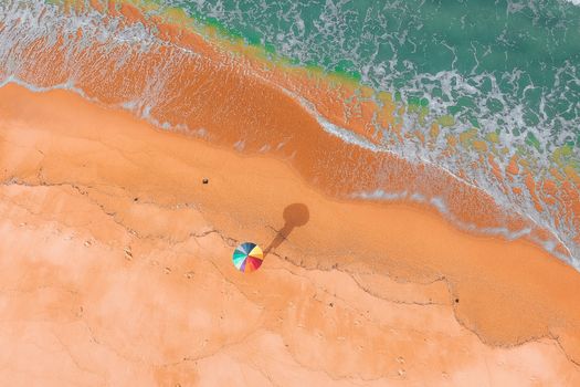 A stunning aerial view of a vibrant beach with a colorful parasol and gentle sea foam washing ashore.