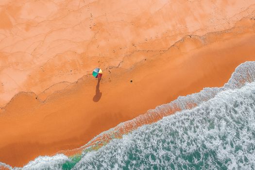 Aerial view of a colorful parasol on a sandy beach with waves crashing on the shore.