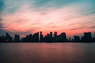 在现代城市中，摩天大楼映衬着令人惊叹的粉红色日落天空，倒映在河水中