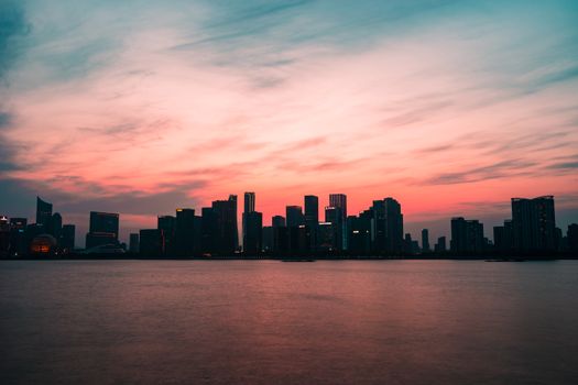 在现代城市中，摩天大楼映衬着令人惊叹的粉红色日落天空，倒映在河水中