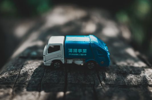 Plastic tiny blue lorry with hieroglyphs on timber bench in sunny shady garden in summer