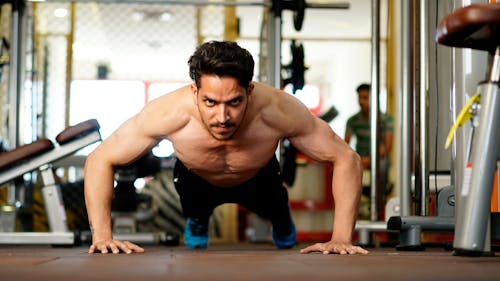 Free Full body of young ethnic serious strong shirtless male athlete doing push ups exercise while training hard in modern gym Stock Photo