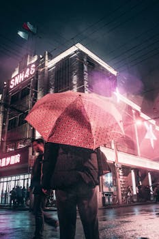 A person holding a pink umbrella on a rainy night in Shanghai's vibrant cityscape.