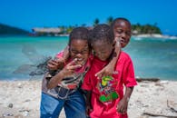 三个快乐的男孩在洪都拉斯海湾群岛阳光明媚的海滩上享受美好时光