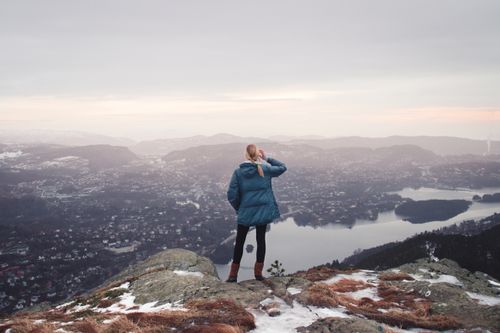 Free A woman stands on a mountain peak, overlooking a vast, scenic winter landscape. Stock Photo